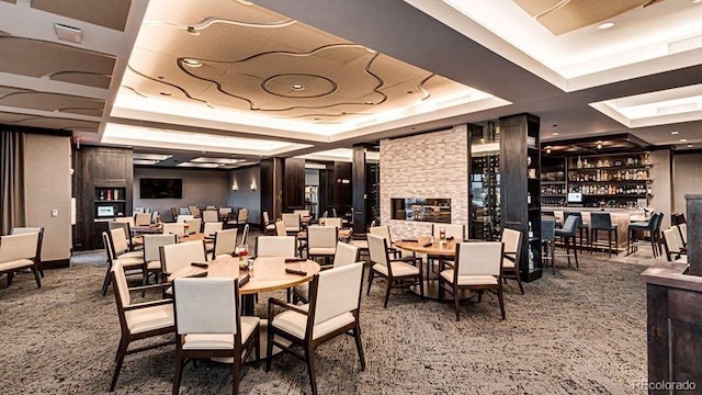 carpeted dining space with a raised ceiling and a community bar