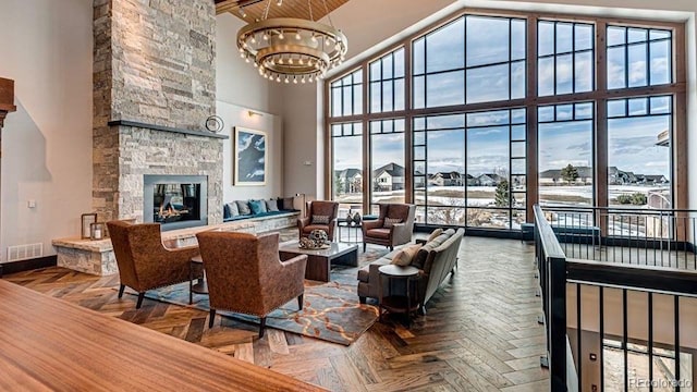 living area featuring baseboards, visible vents, an inviting chandelier, a stone fireplace, and a towering ceiling