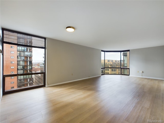 unfurnished room featuring light wood-type flooring, floor to ceiling windows, baseboards, and a view of city