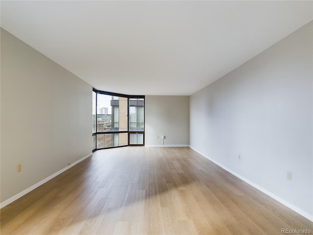 empty room with a wall of windows, light wood-style flooring, and baseboards