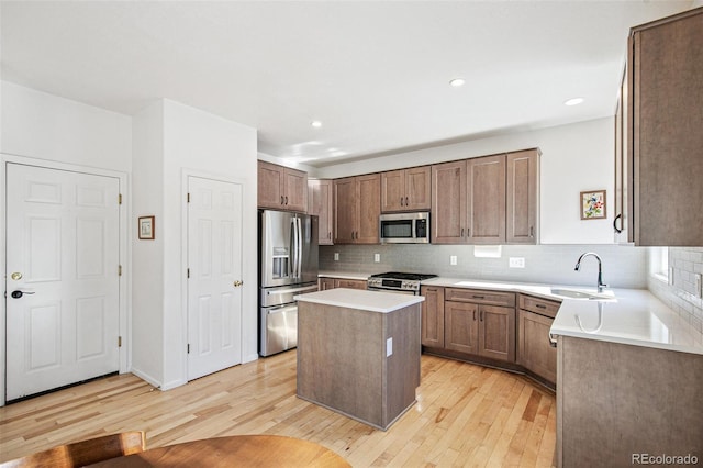 kitchen with sink, tasteful backsplash, light hardwood / wood-style flooring, a kitchen island, and stainless steel appliances