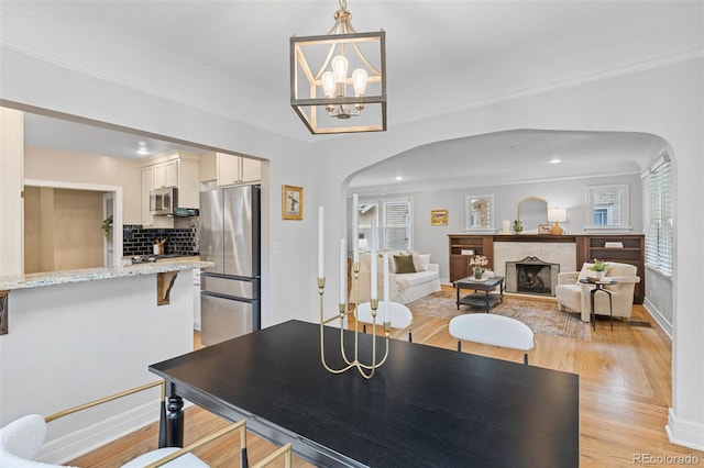 3334 W 37th Ave, Denver, CO 80211 - dining area with arched walkways, light wood finished floors, a tiled fireplace, ornamental molding, and a chandelier