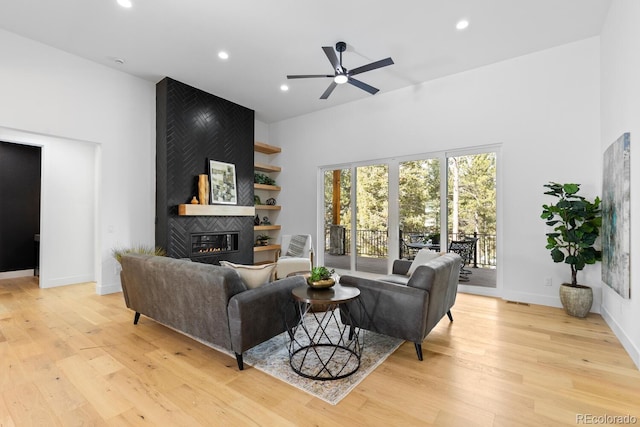 living room featuring light hardwood / wood-style flooring, a large fireplace, ceiling fan, and a high ceiling