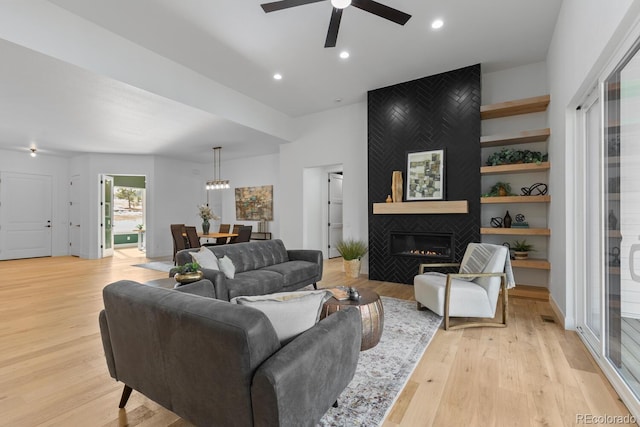 living room with built in features, light hardwood / wood-style floors, a large fireplace, and ceiling fan