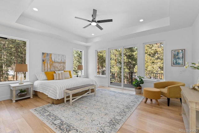 bedroom with a tray ceiling, light hardwood / wood-style flooring, and access to outside