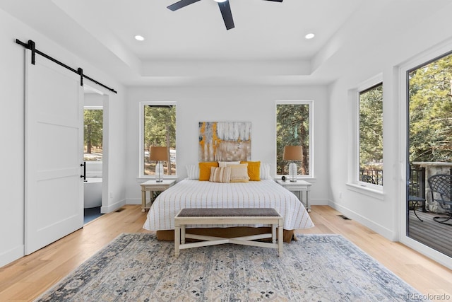 bedroom with a barn door, a raised ceiling, access to exterior, and light wood-type flooring