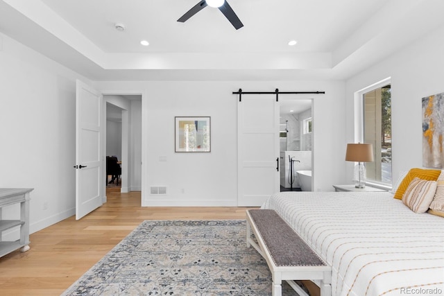 bedroom featuring ensuite bathroom, a barn door, a raised ceiling, and light hardwood / wood-style floors