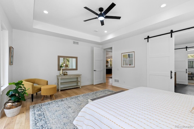 bedroom with hardwood / wood-style flooring, a barn door, and a raised ceiling