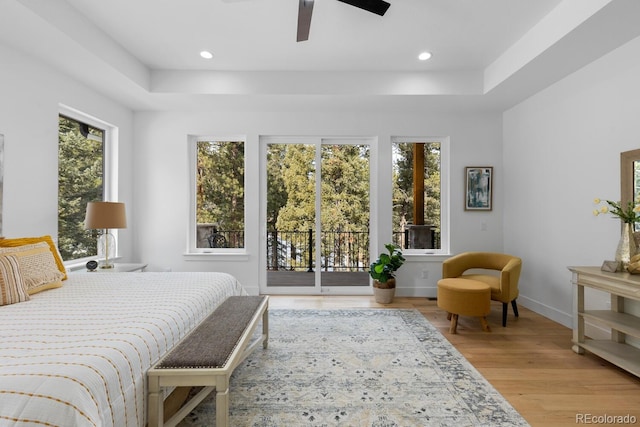 bedroom featuring ceiling fan, access to exterior, a raised ceiling, and light hardwood / wood-style flooring