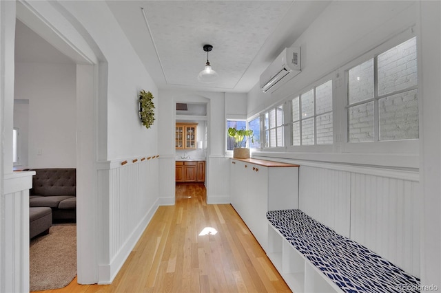 hallway with a decorative wall, wainscoting, light wood finished floors, and a wall mounted air conditioner