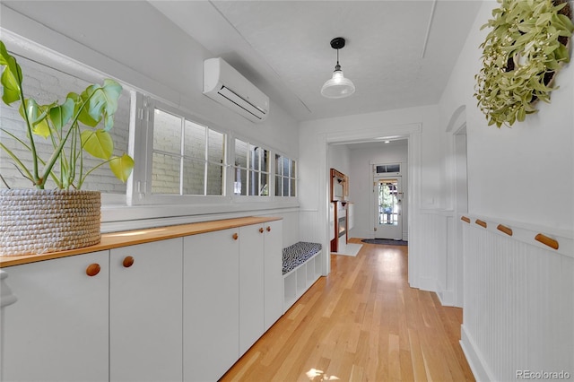 hall featuring light wood-style floors, a wainscoted wall, a decorative wall, and a wall mounted air conditioner
