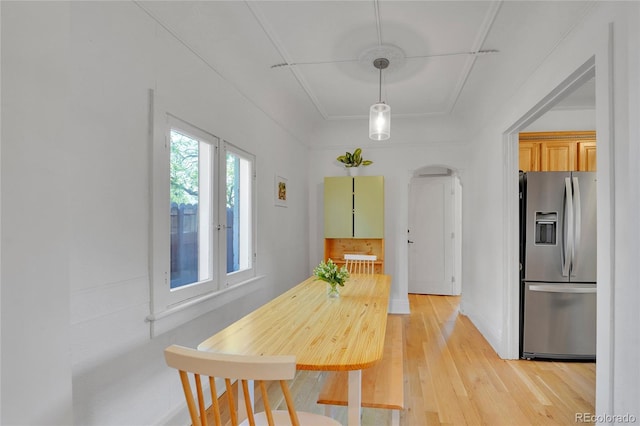 dining space featuring light wood-style floors, arched walkways, and baseboards