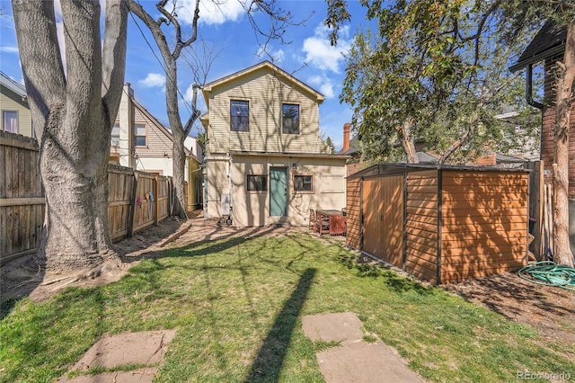 back of house with a yard, an outdoor structure, a fenced backyard, and a storage unit