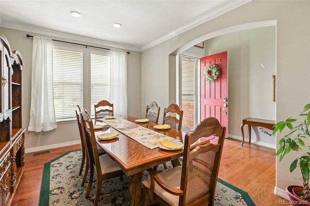 dining area with baseboards, light wood-type flooring, ornamental molding, visible vents, and arched walkways
