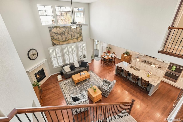 living room with ceiling fan, a high ceiling, wood finished floors, a tiled fireplace, and baseboards