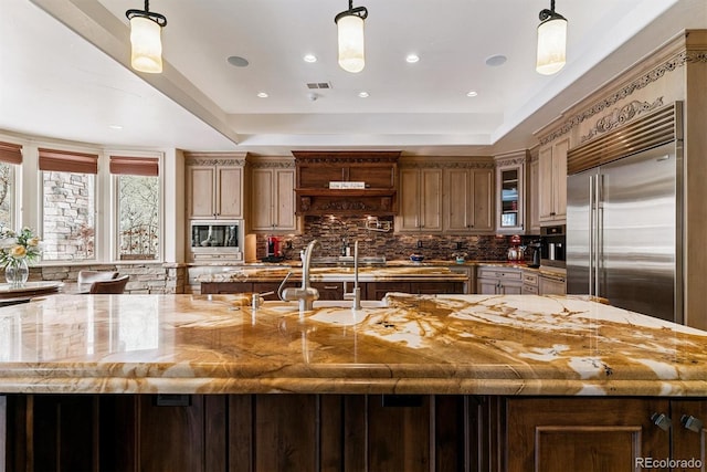 kitchen featuring decorative backsplash, built in appliances, a tray ceiling, and a sink