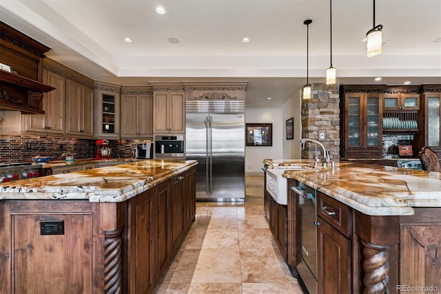kitchen featuring stainless steel appliances, a sink, a spacious island, light stone countertops, and tasteful backsplash