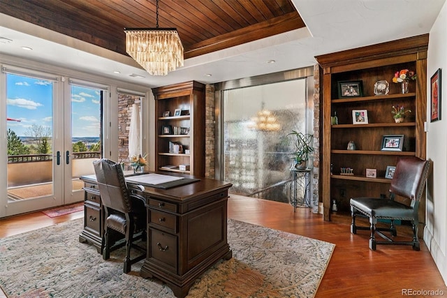 office space with an inviting chandelier, a raised ceiling, wood finished floors, wooden ceiling, and french doors