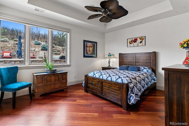 bedroom with a tray ceiling, wood finished floors, visible vents, and baseboards