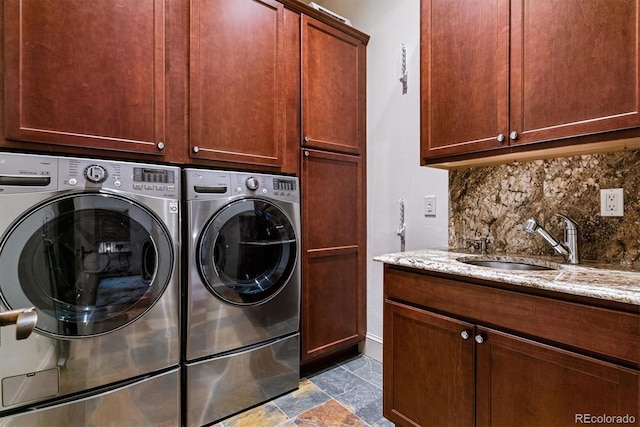 clothes washing area featuring stone finish flooring, cabinet space, washer and clothes dryer, and a sink