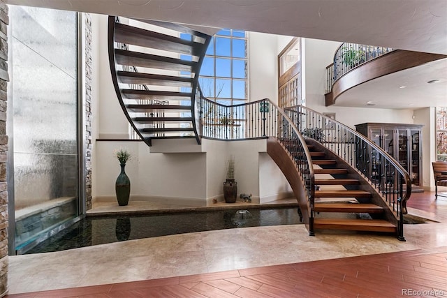 staircase featuring a towering ceiling, wood finished floors, and baseboards
