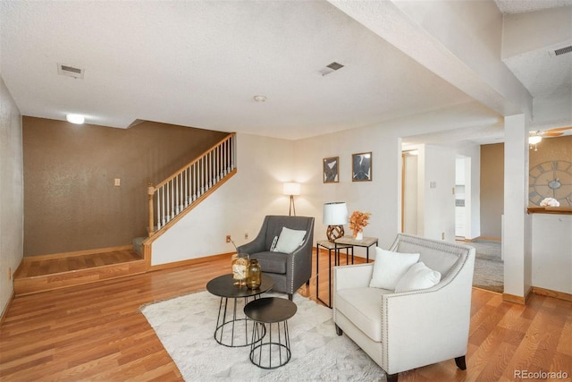 sitting room with stairs, light wood finished floors, baseboards, and a ceiling fan