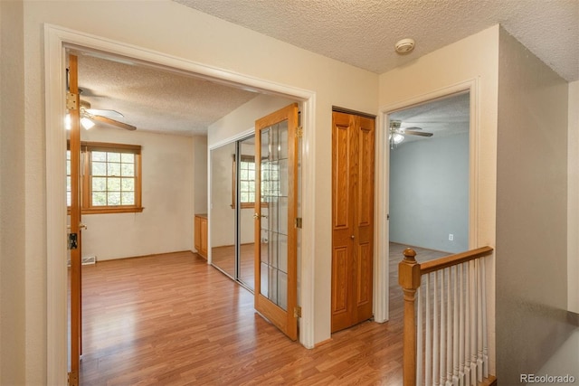 hallway featuring a textured ceiling, wood finished floors, and an upstairs landing