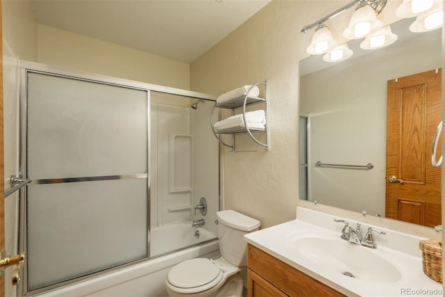 bathroom featuring a textured wall, toilet, combined bath / shower with glass door, and vanity
