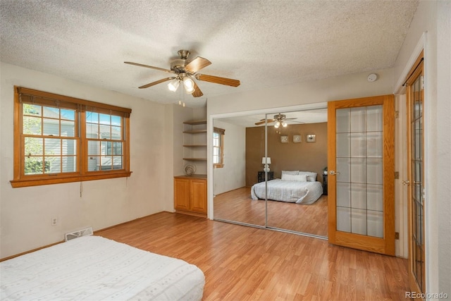 bedroom featuring light wood-type flooring, a textured ceiling, a closet, a ceiling fan, and french doors