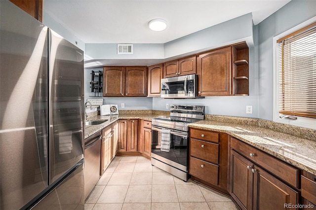 kitchen with sink, light tile patterned flooring, light stone counters, and appliances with stainless steel finishes