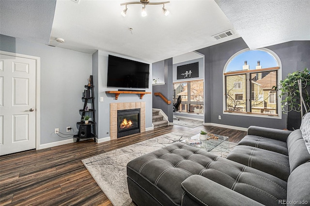 living room featuring a textured ceiling, a tiled fireplace, and dark hardwood / wood-style floors