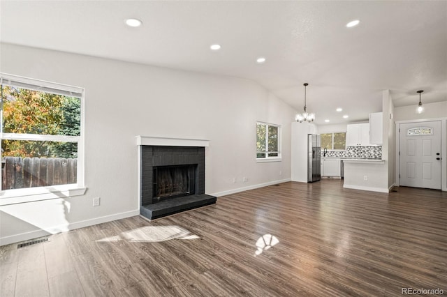 unfurnished living room featuring an inviting chandelier, lofted ceiling, a brick fireplace, and dark hardwood / wood-style floors