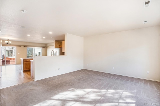 unfurnished living room with a notable chandelier, light colored carpet, visible vents, and baseboards