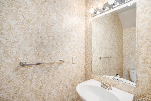 bathroom featuring a sink, toilet, and wallpapered walls