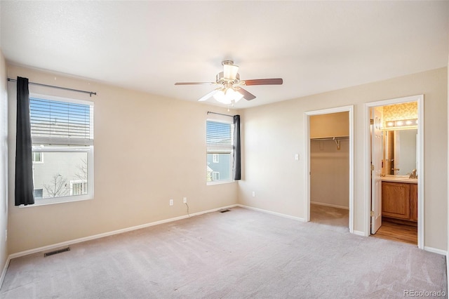 unfurnished bedroom with a spacious closet, visible vents, connected bathroom, baseboards, and light colored carpet