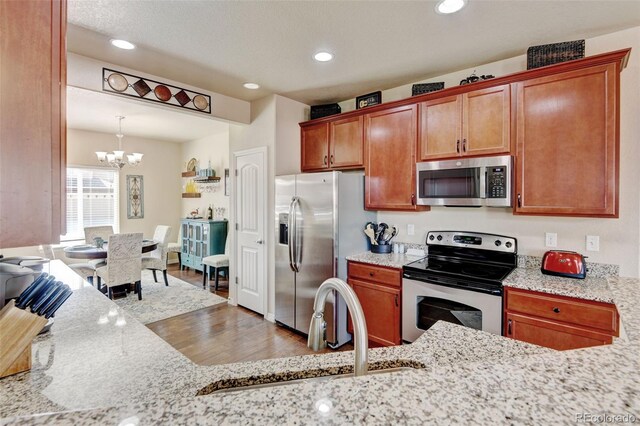 9046 Sandpiper Dr, Frederick, CO 80504 - kitchen with stainless steel appliances, a chandelier, a sink, wood finished floors, and brown cabinets