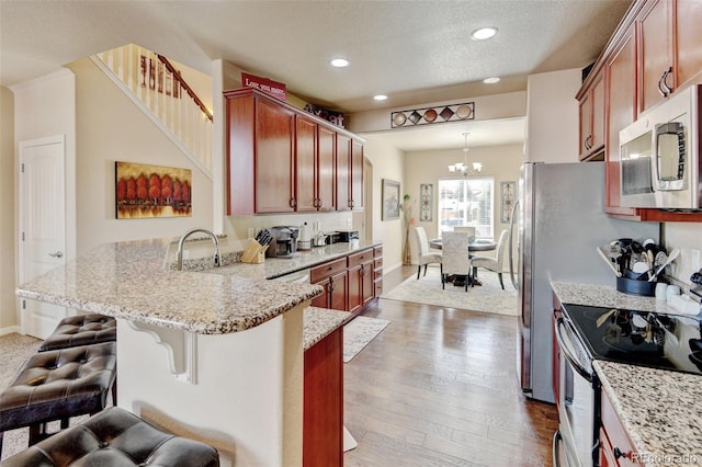 9046 Sandpiper Dr, Frederick, CO 80504 - kitchen featuring appliances with stainless steel finishes, a peninsula, light stone countertops, a chandelier, and recessed lighting