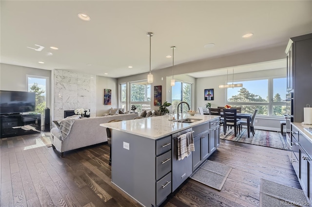 kitchen featuring stainless steel dishwasher, sink, a tile fireplace, pendant lighting, and an island with sink