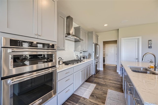 kitchen featuring light stone countertops, sink, wall chimney exhaust hood, gray cabinets, and appliances with stainless steel finishes