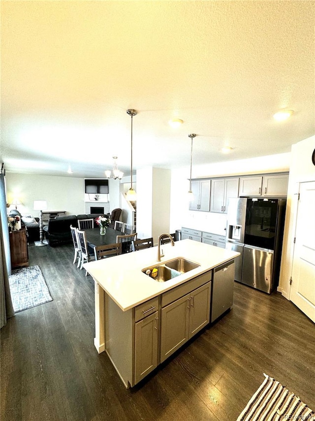 kitchen with a kitchen island with sink, a sink, light countertops, appliances with stainless steel finishes, and decorative light fixtures