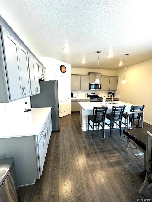 kitchen with appliances with stainless steel finishes, pendant lighting, light countertops, and gray cabinets