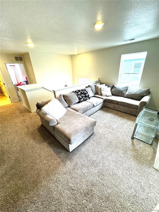 living area with a wealth of natural light, carpet flooring, visible vents, and a textured ceiling