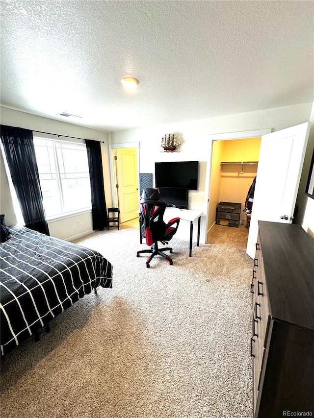 bedroom with a spacious closet, visible vents, a textured ceiling, and light colored carpet