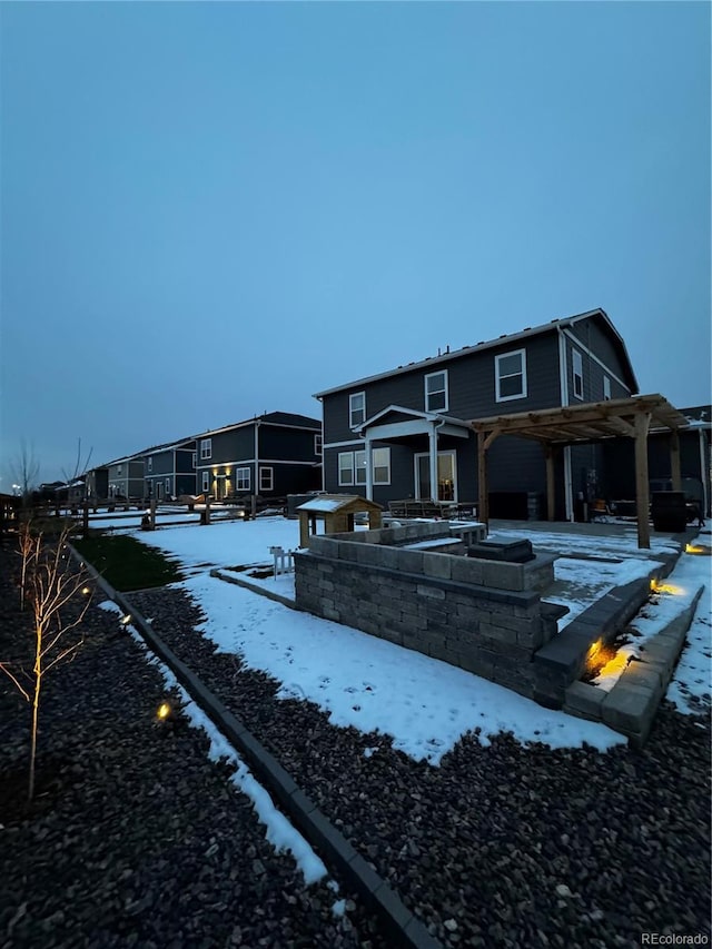 snow covered back of property featuring a residential view and a pergola