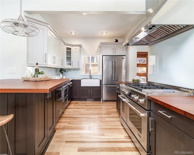 kitchen featuring white cabinetry, wood counters, glass insert cabinets, and high end appliances