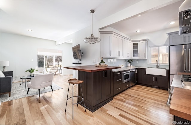 kitchen featuring glass insert cabinets, built in appliances, a kitchen bar, white cabinetry, and a sink