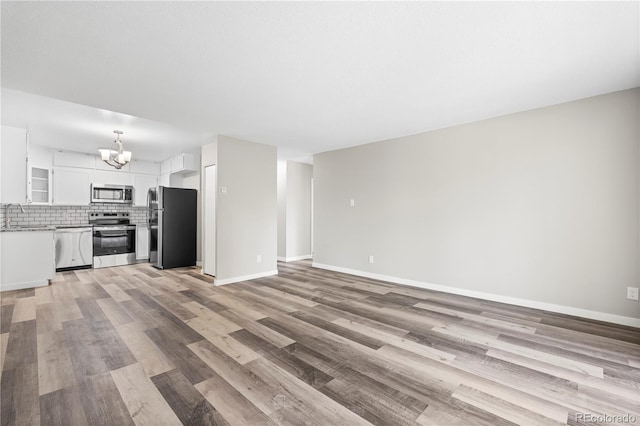 unfurnished living room with an inviting chandelier, baseboards, light wood finished floors, and a sink
