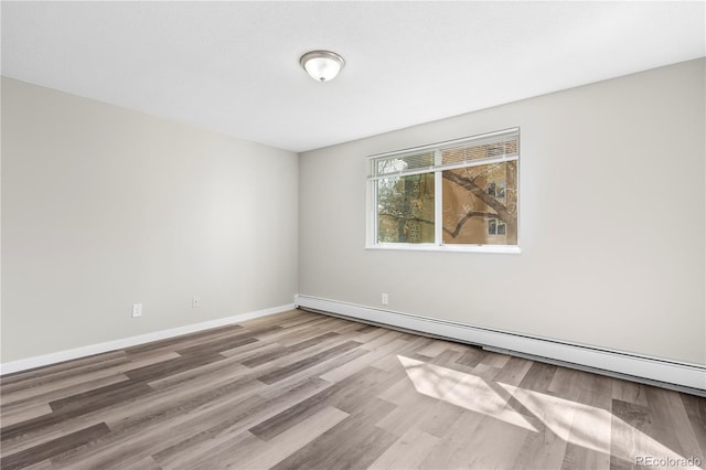 empty room with wood finished floors, baseboards, and a baseboard heating unit