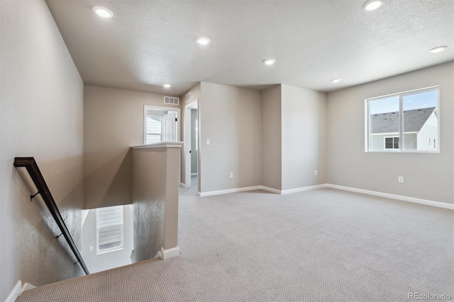 spare room featuring a textured ceiling, light carpet, and a wealth of natural light