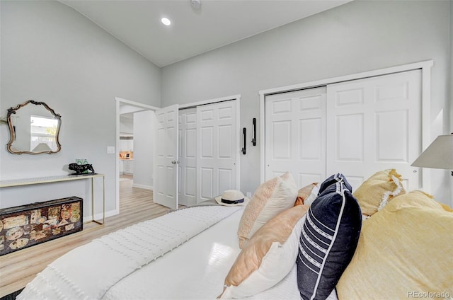 bedroom with two closets, light hardwood / wood-style floors, and high vaulted ceiling